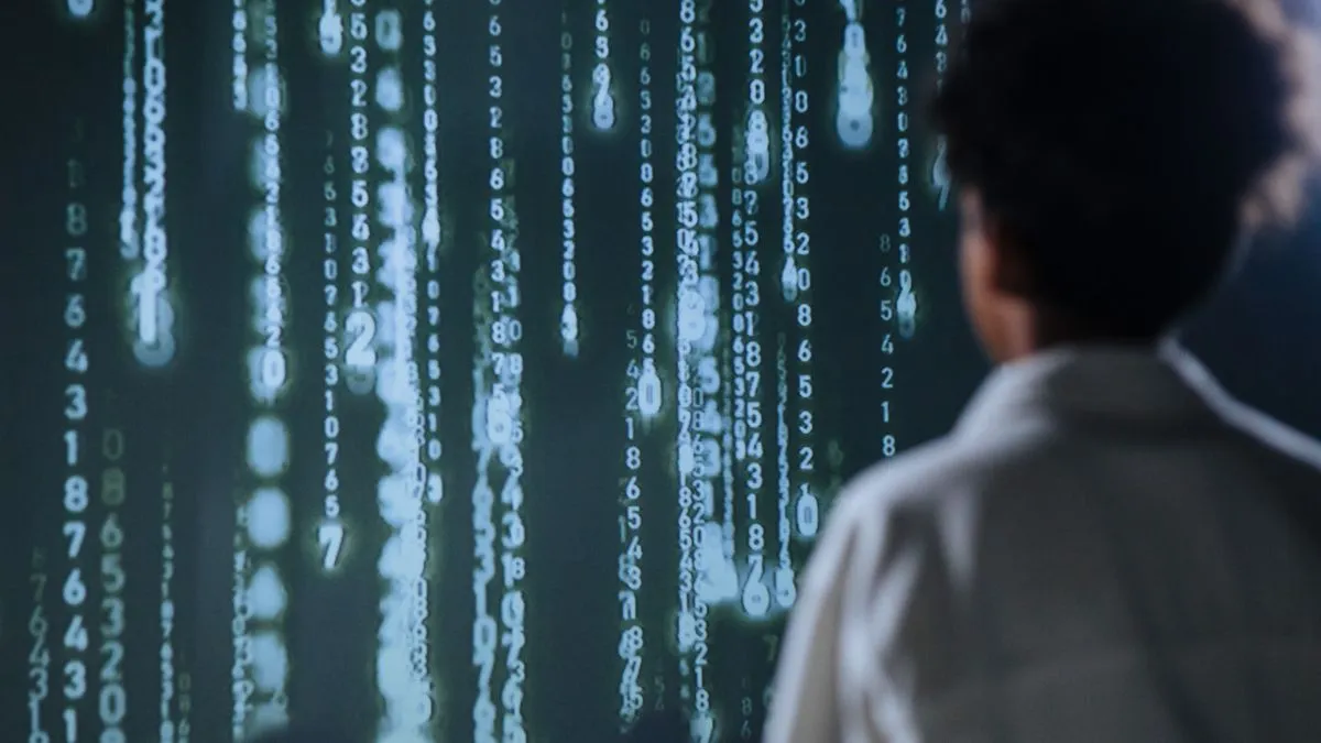 A person seen from behind faces a large dark screen filled with glowing columns of falling numbers.
