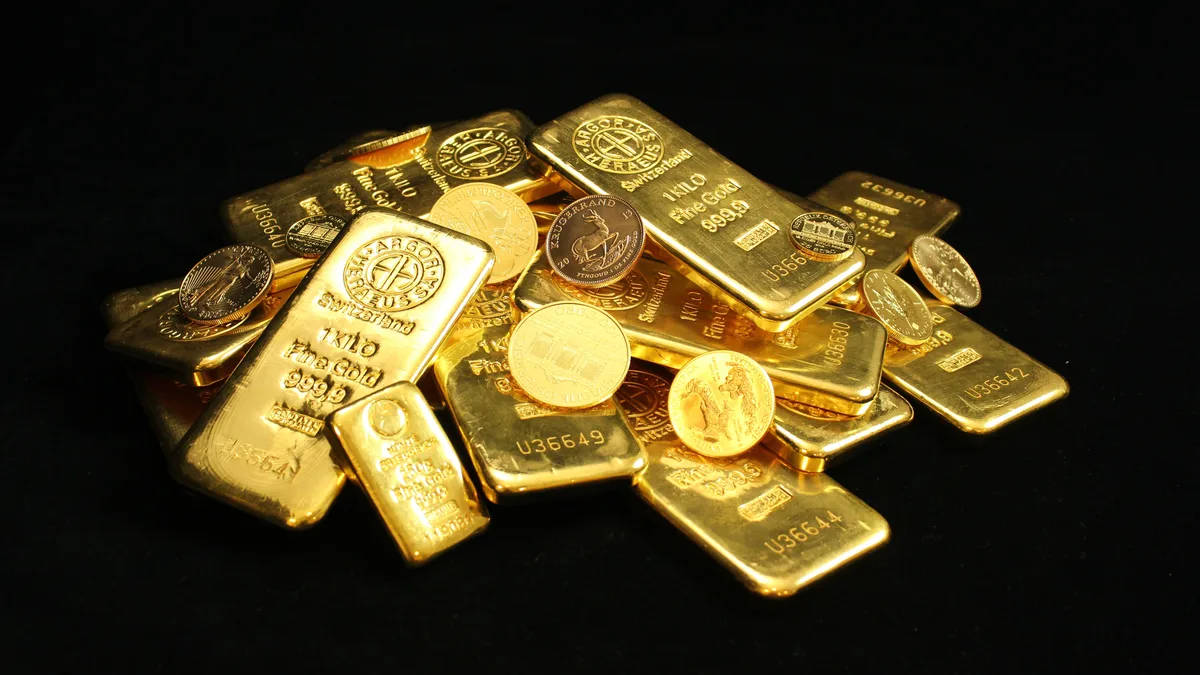 如何投资黄金:实物、ETF与采矿股 A stack of gold bullion bars and coins in a vault, physical gold you must store and insure