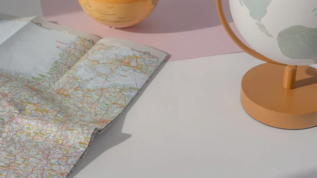 An unfolded road map lying next to a small desk globe on a pastel pink and white tabletop.