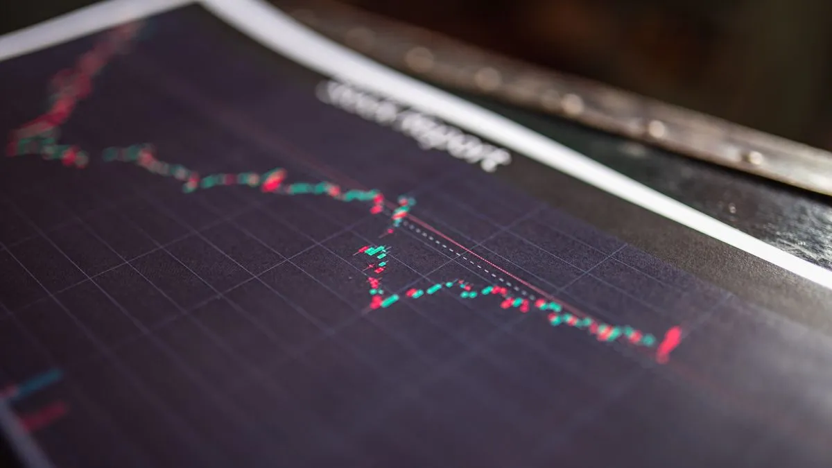 A printed page with a red and green candlestick chart on a dark background, lying on a desk in low side light.