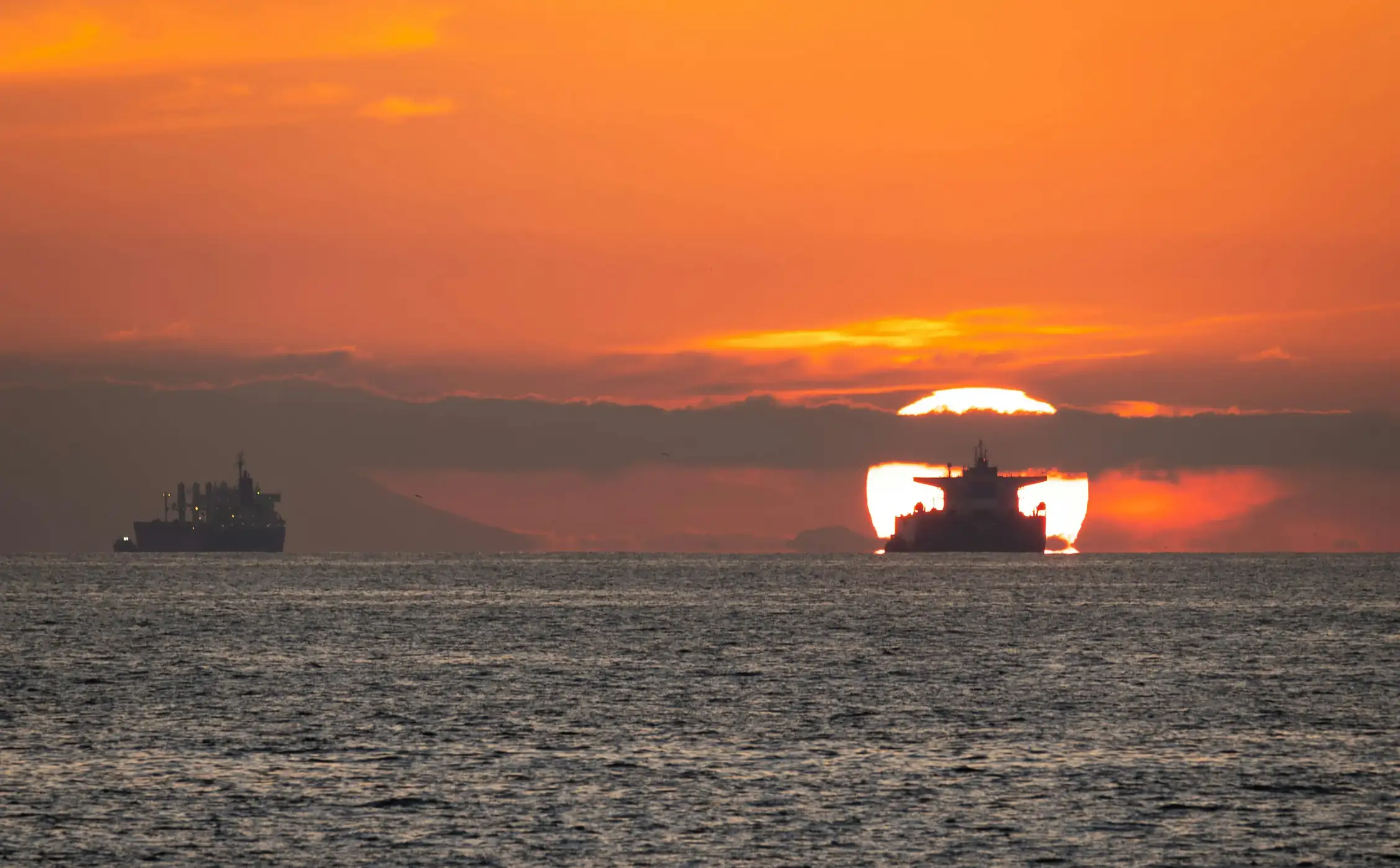 Naval warships providing security escort for commercial vessels in the Strait of Hormuz at sunset