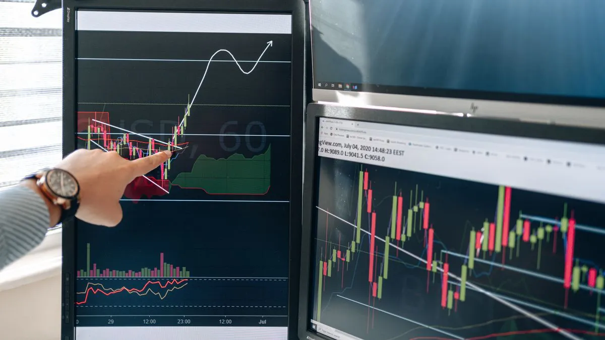 期权希腊字母详解:Delta、Gamma、Theta 和 Vega A hand with a wristwatch points at an upward arrow sketched over a candlestick chart on a vertical monitor, with more charts on a screen behind.