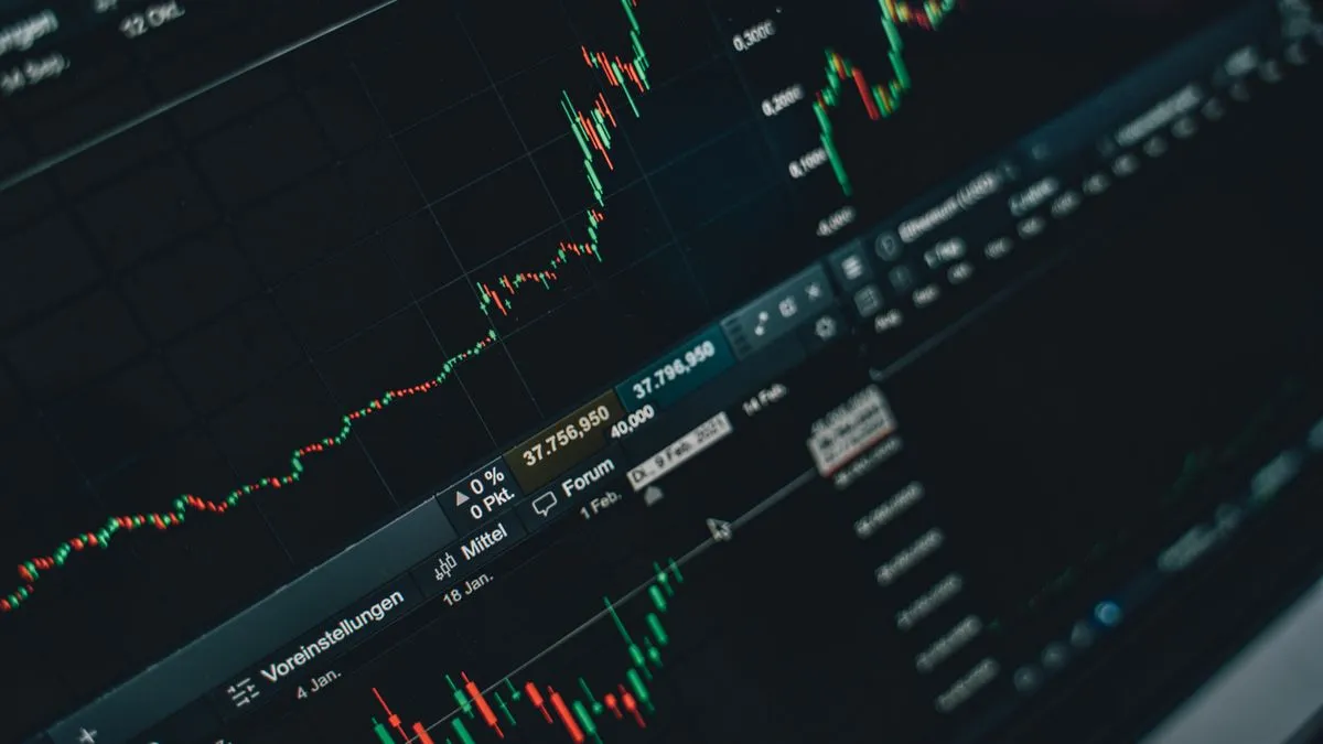 A monitor displays green and red candlestick stock charts with price levels and trading platform menus.