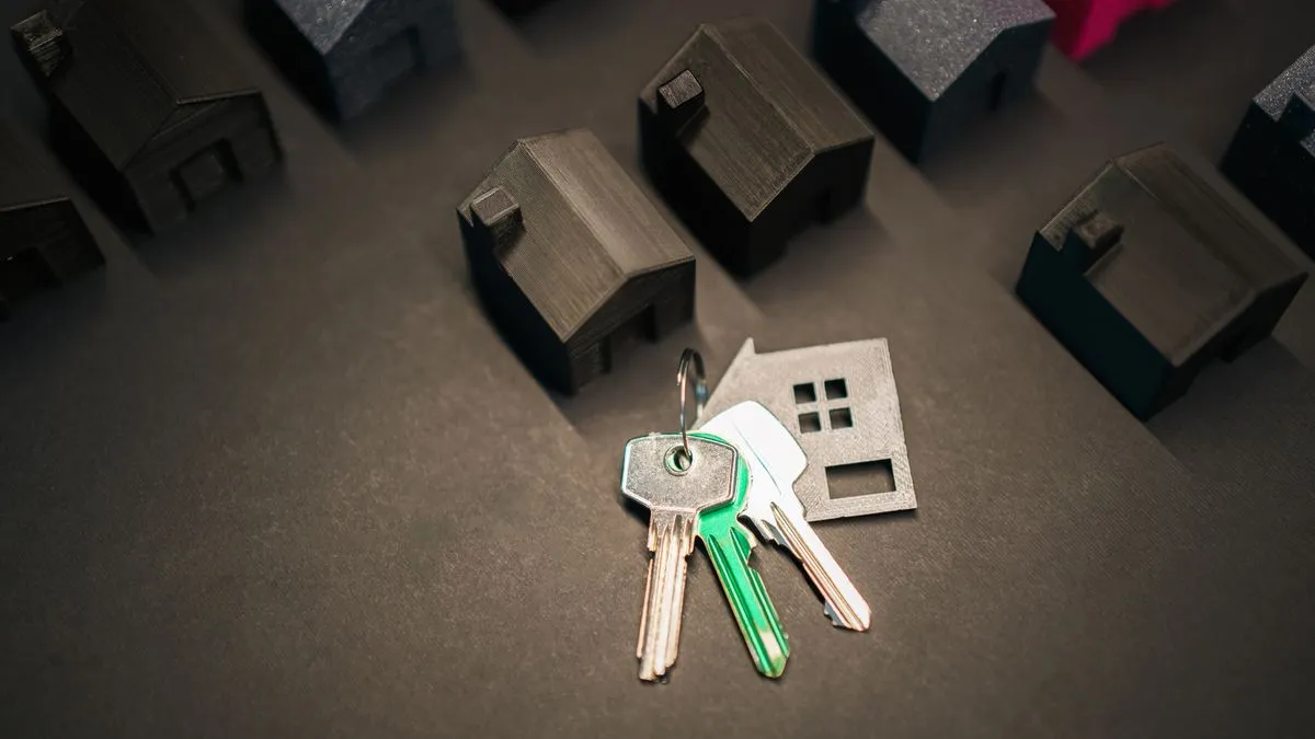Rent vs buy: the math that actually decides it A set of keys with a metal house-shaped keyring lies on a dark surface between rows of small black model houses.