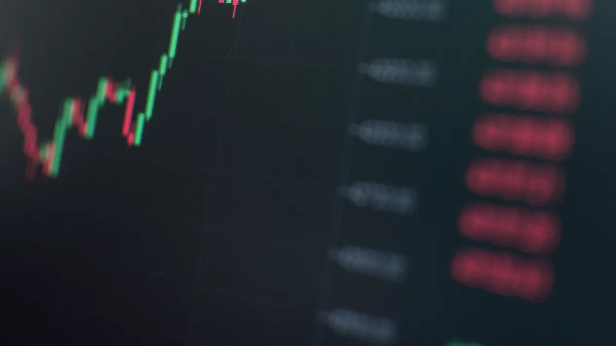 A dark trading screen shows green and red candlesticks beside a column of falling price quotes.