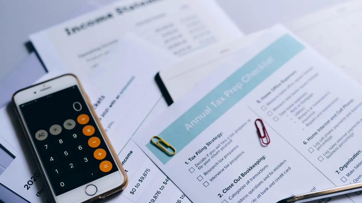Vorabpauschale bei thesaurierenden ETFs erklärt A smartphone calculator rests on spread-out tax paperwork, including an annual tax preparation checklist and income statements.